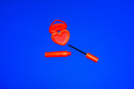 Red heart shape makeup compact and mascara on blue background