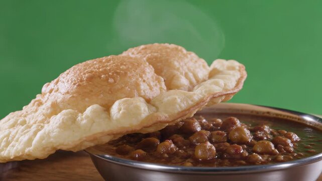 Steaming golden Bhatura and dark Chole curry, isolated on a bright green