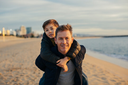Portrait of father carrying son piggyback on the beach