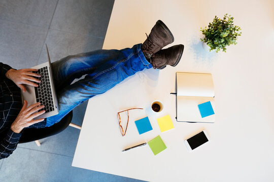 Businessman using laptop with feet on desk in office