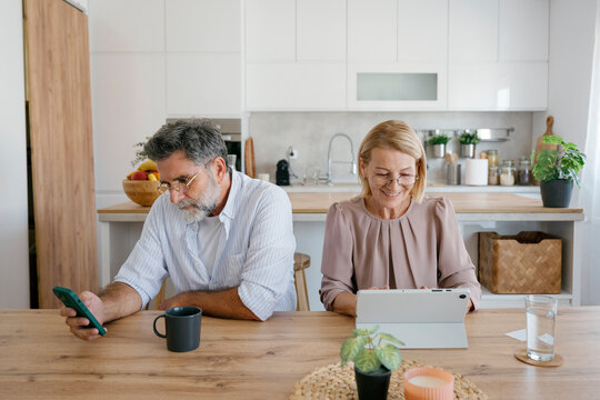 Married couple sitting at home using digital tablet and smartphone