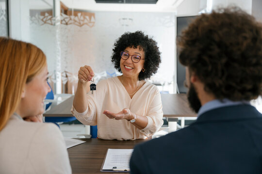 Real estate agent giving keys to couple after contract signing