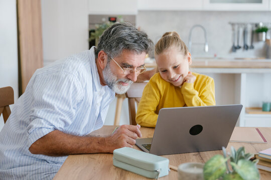 Grandfather and child learning together at laptop in kitchen