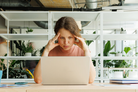 Stressed businesswoman works on laptop at modern office desk