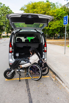 Woman in wheelchair loading electric handbike into adapted van at accessible parking