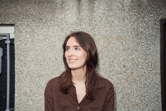 A smiling woman wears a brown shirt outdoors