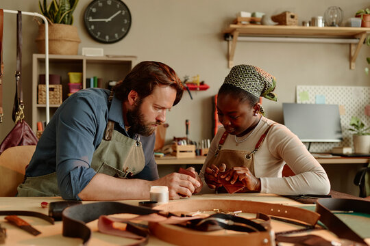 Man and woman craft leather goods together in a workshop
