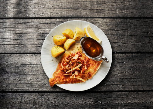 Fried plaice with potatoes and butter sauce on a wooden table