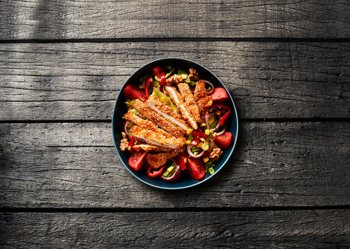 A fresh chicken salad sits on a dark wooden table