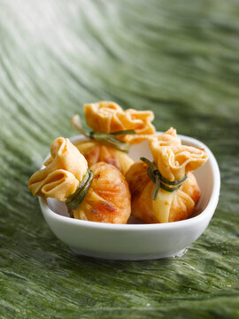 Three fried dim sum dumplings sit in a white bowl on a green leaf