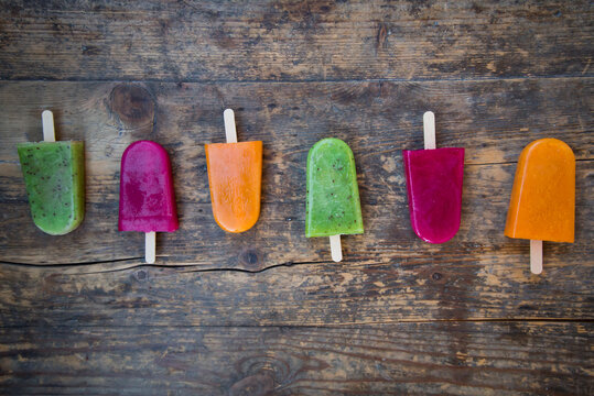 Row of fruit smoothie ice lollies on dark wood