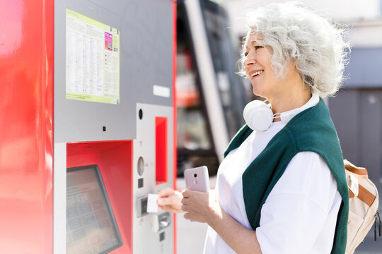 Mature woman buys a ticket at the bus stop using a machine