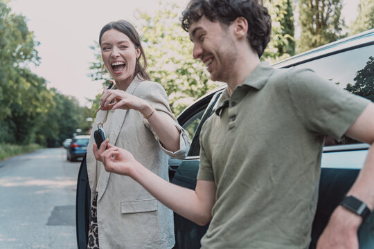 Laughing woman gives a car key to a man outdoors
