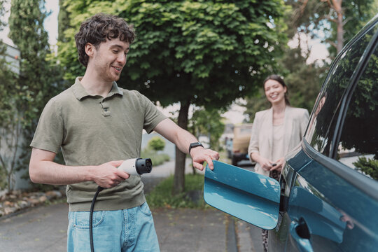 Man charges electric car at home while woman smiles