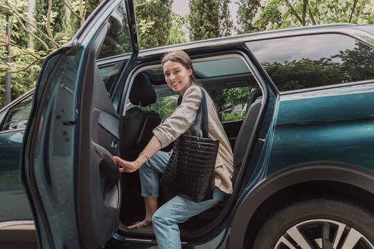 A smiling woman enters a car holding a black bag