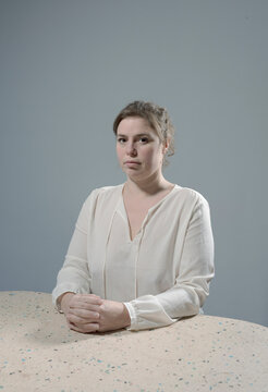 Woman sitting upright at table with serious expression indoors