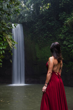 Woman in red dress admires a jungle waterfall in Bali