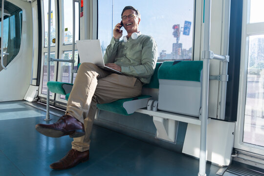 Smiling businessman works on laptop and talks on phone in tram