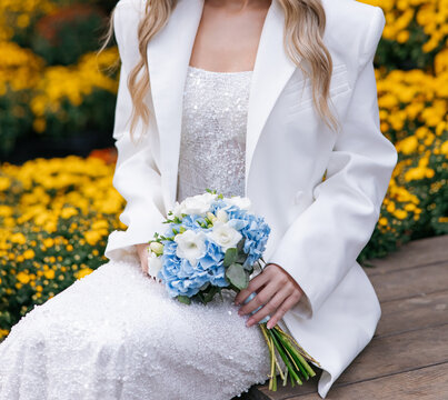 Bride holding wedding bouquet sitting on bench outdoors