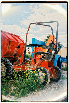 An abandoned orange tractor sits among wildflowers in the countryside