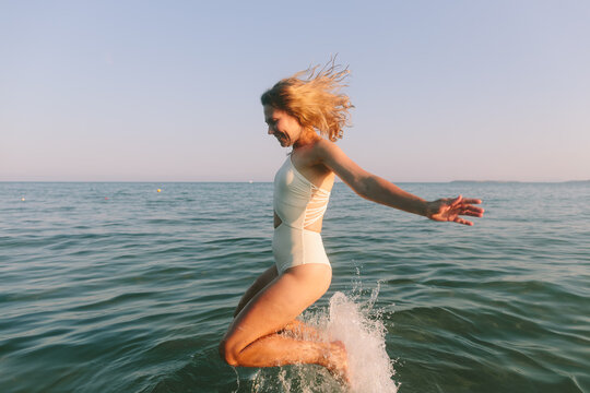 Happy woman in swimsuit jumping in the sea enjoying summer freedom