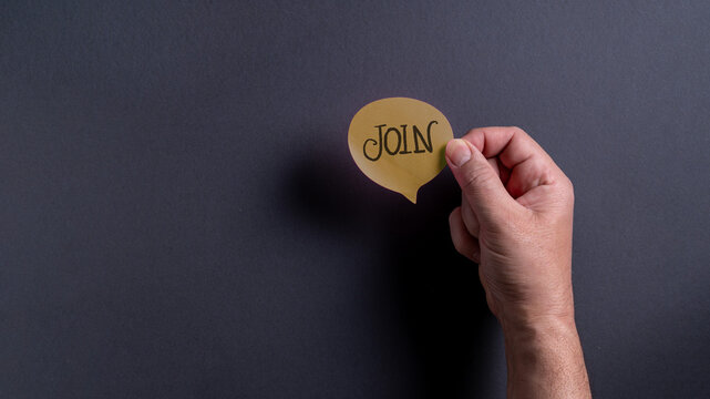 Male hand holding brown speech bubble with join text on dark background