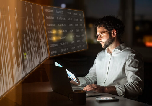 Businessman analyzes financial chart on laptop at night in office