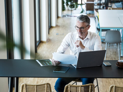 Smiling businessman reads document at his modern office desk