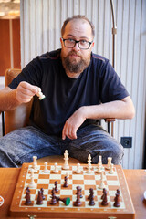 Man with glasses plans chess strategy during peaceful afternoon indoor. Contemplative Caucasian man wearing glasses carefully evaluates chess positions indoors in calm afternoon setting © anatoliy_gleb