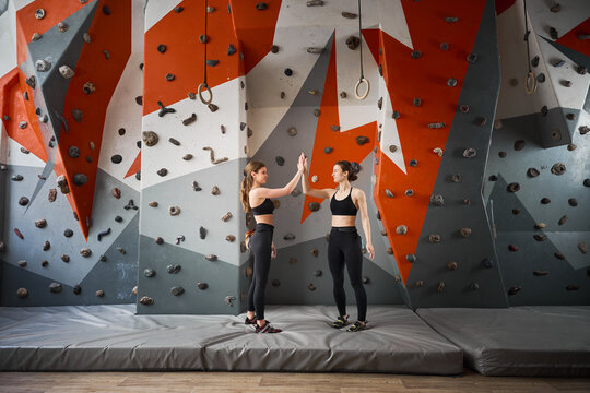 Women celebrate training progress with high five in climbing gym. Photo for support, partnership, achievement, wellness, sport marketing, gym advertising