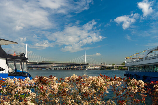 Panoramic view of the Halic Metro Bridge in istanbul with white flowers and passenger ferries on the water under a blue sky