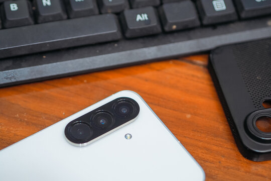 close-up view of the rear camera setup on a white smartphone placed on a wooden table beside a computer keyboard.