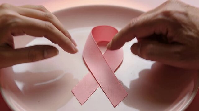 Approaching fingers smoothing and aligning pink awareness ribbon on shallow plate, securing shape