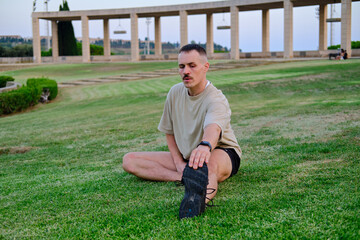 Fototapeta premium front view of Man stretching leg on grass in park