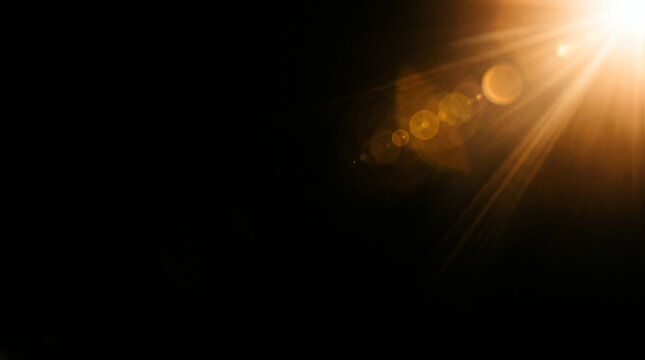 Bright golden lens flare glowing optical light leak shining sunbeam rays with round bokeh circles over pitch black background overlay texture