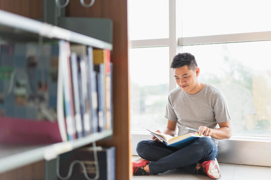 male asian student studying and reading book in library
