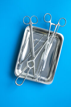 Sterile surgical instruments and tools - scalpels, scissors and others - in a stainless tray on blue background, top view