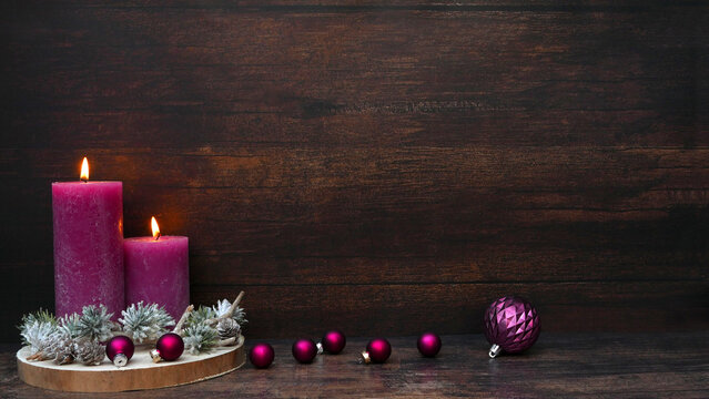 A festive Christmas background featuring two purple candles and Christmas baubles set against dark wood, with space for text.

