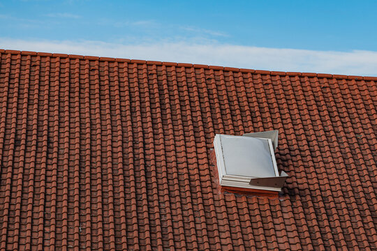 A rooftop with window covered in terracotta tiles under blue sky