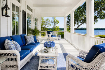 Fototapeta premium An outdoor patio area with white columns, wicker furniture, and blue cushions overlooking a body of water.