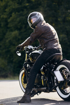 Rider in leather jacket and helmet posing on a custom vintage motorbike outdoors, enjoying the open road and freedom