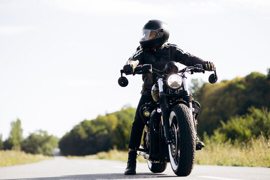 Biker wearing a helmet and leather jacket riding a custom motorcycle on an open road, embodying adventure and independence