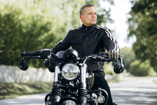 Man in leather jacket and gloves sitting on a motorcycle, looking forward, enjoying a ride and the journey outdoors
