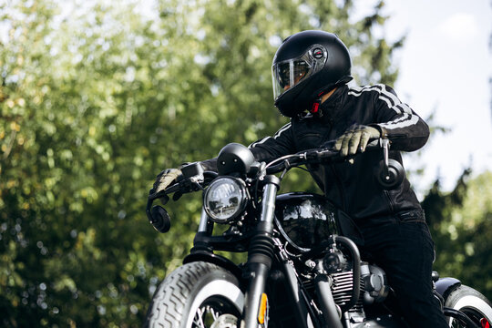 Biker wearing a black helmet and leather jacket, sitting on a vintage cafe racer motorcycle, enjoying freedom and adventure