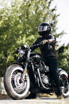 Biker wearing helmet and leather jacket on a black custom bobber motorcycle, enjoying the journey and freedom outdoors