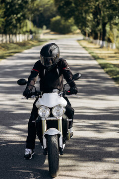 Biker wearing helmet and protective gear riding a white modern motorcycle on an empty road during a daytime outdoor trip