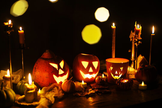Jack o lantern glowing pumpkins, spooky spiders and burning candles on dark moody background. Happy Halloween. Spooky atmospheric halloween night, space for text. Trick or treat