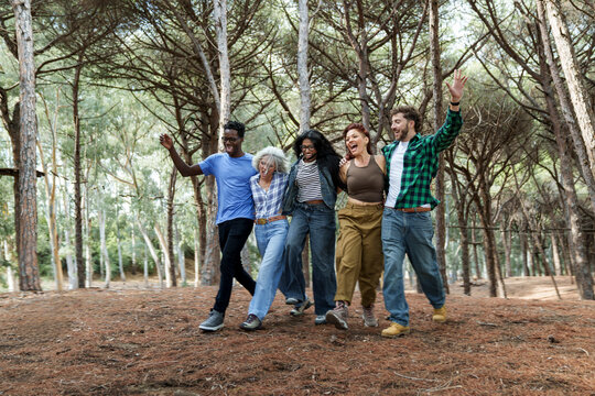 Friends laughing and jumping together with arms around each other in a forest