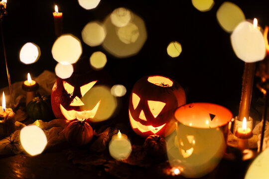 Happy Halloween. Jack o lantern glowing pumpkins, spooky spiders and burning candles on dark moody background. Spooky atmospheric halloween night, space for text. Trick or treat
