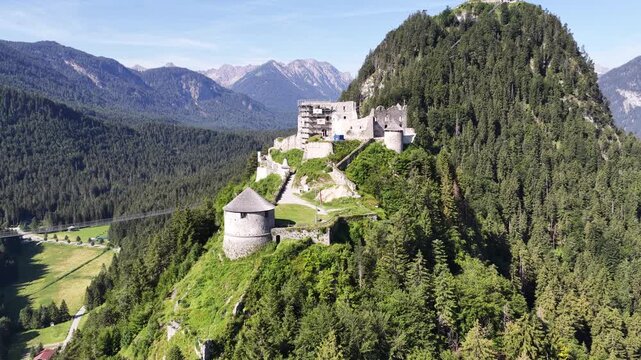 Ehrenberg castle ruins and watchtower orbit into view near Reutte, Austria, aerial drone orbit around fortress, bridge and Tirol Alps.